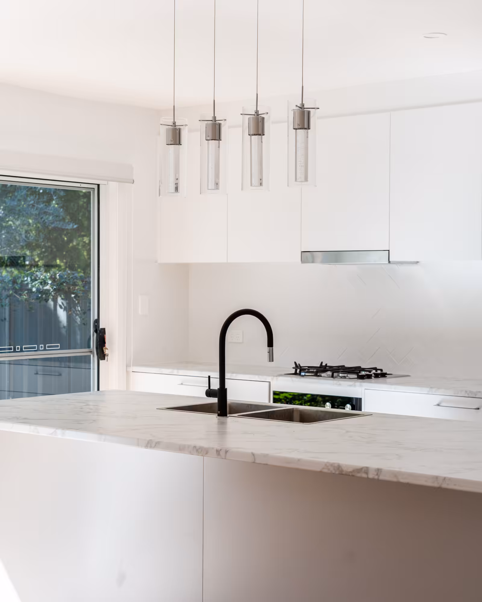 White modern kitchen with marble island bench and pendant lighting and outdoor garden view